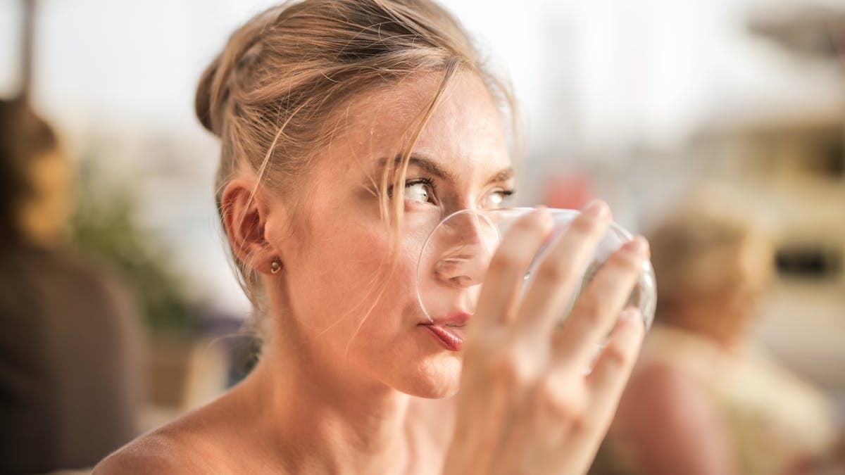 Close-up portrait of a woman drinking from a glass in a soft lighting setting.